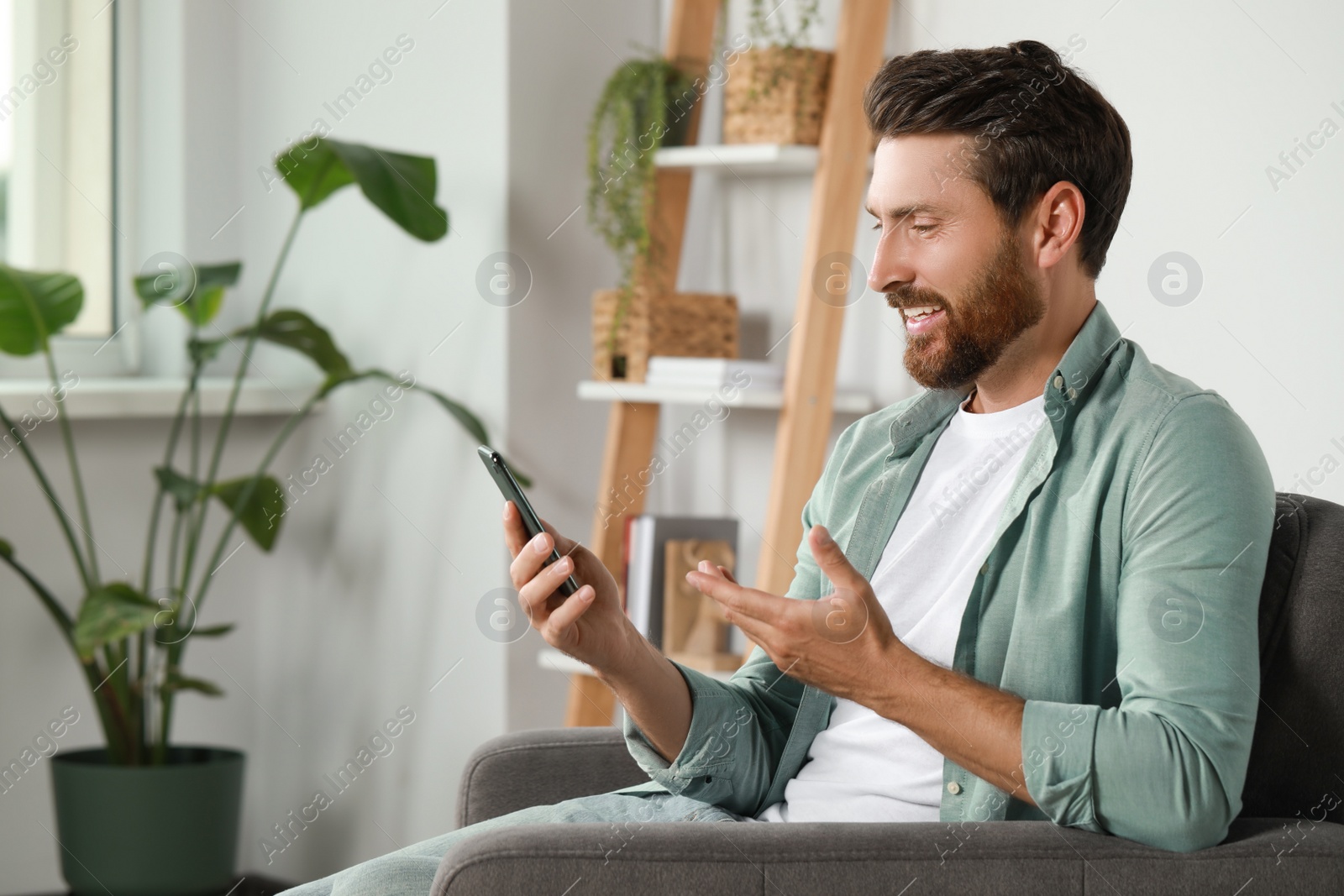 Photo of Handsome man with smartphone having video chat at home, space for text