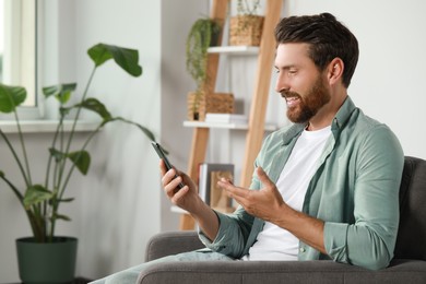 Handsome man with smartphone having video chat at home, space for text