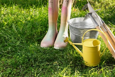 Watering can, gardening tools and rubber boots on green grass outdoors