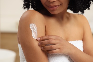 Photo of Young woman applying body cream onto arm indoors, closeup