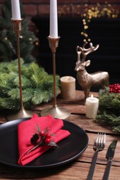 Photo of Plate with red fabric napkin, cutlery and festive decor on wooden table