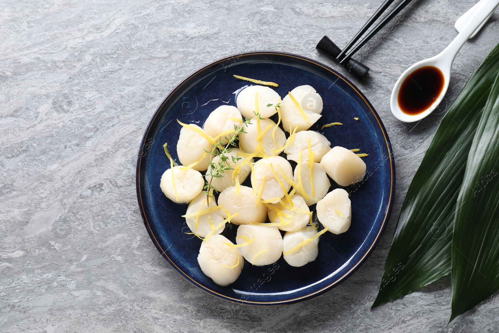 Photo of Raw scallops with thyme and lemon zest served on grey marble table, flat lay. Space for text