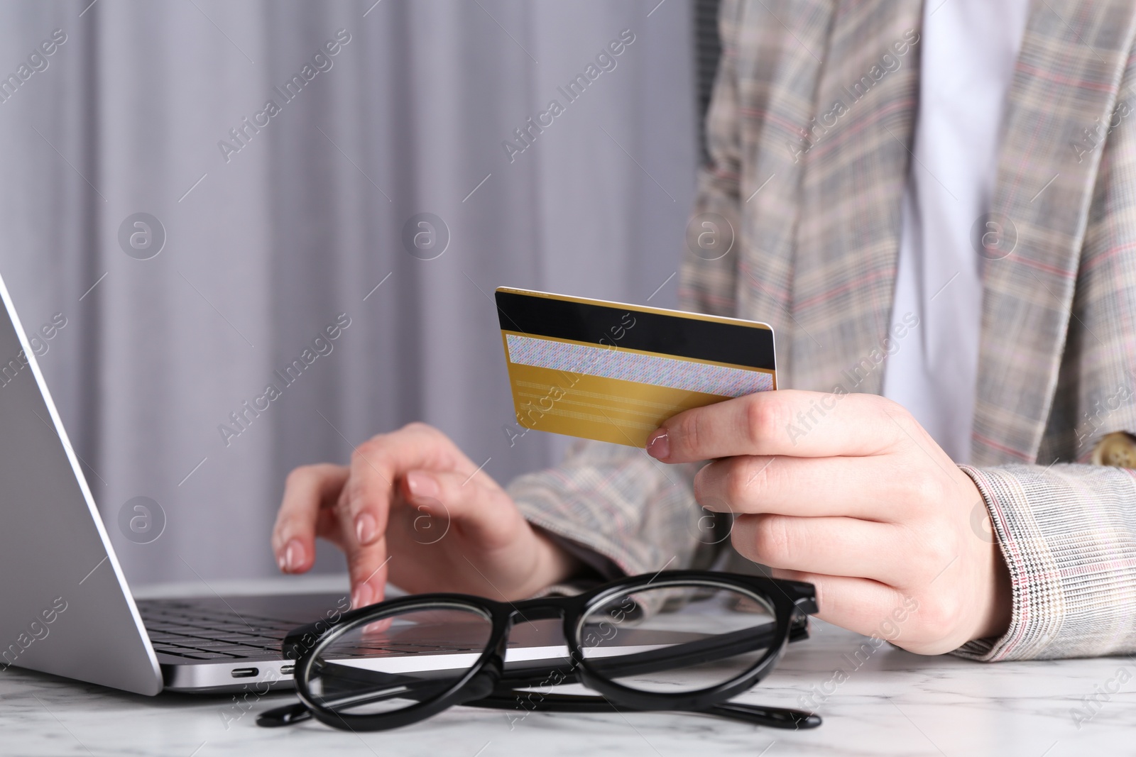 Photo of Online payment. Woman with laptop and credit card at white marble table, closeup