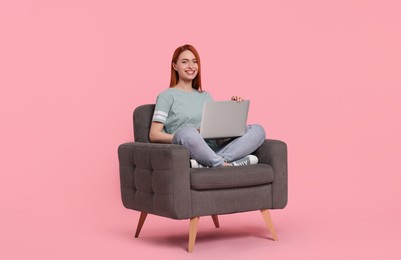 Photo of Smiling young woman with laptop sitting in armchair on pink background