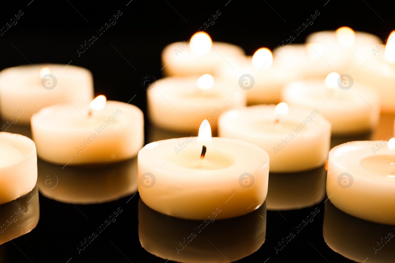 Photo of Wax candles burning on table in darkness, closeup