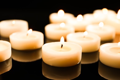 Photo of Wax candles burning on table in darkness, closeup