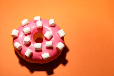 Photo of Sweet delicious glazed donut decorated with marshmallow on orange background, above view. Space for text