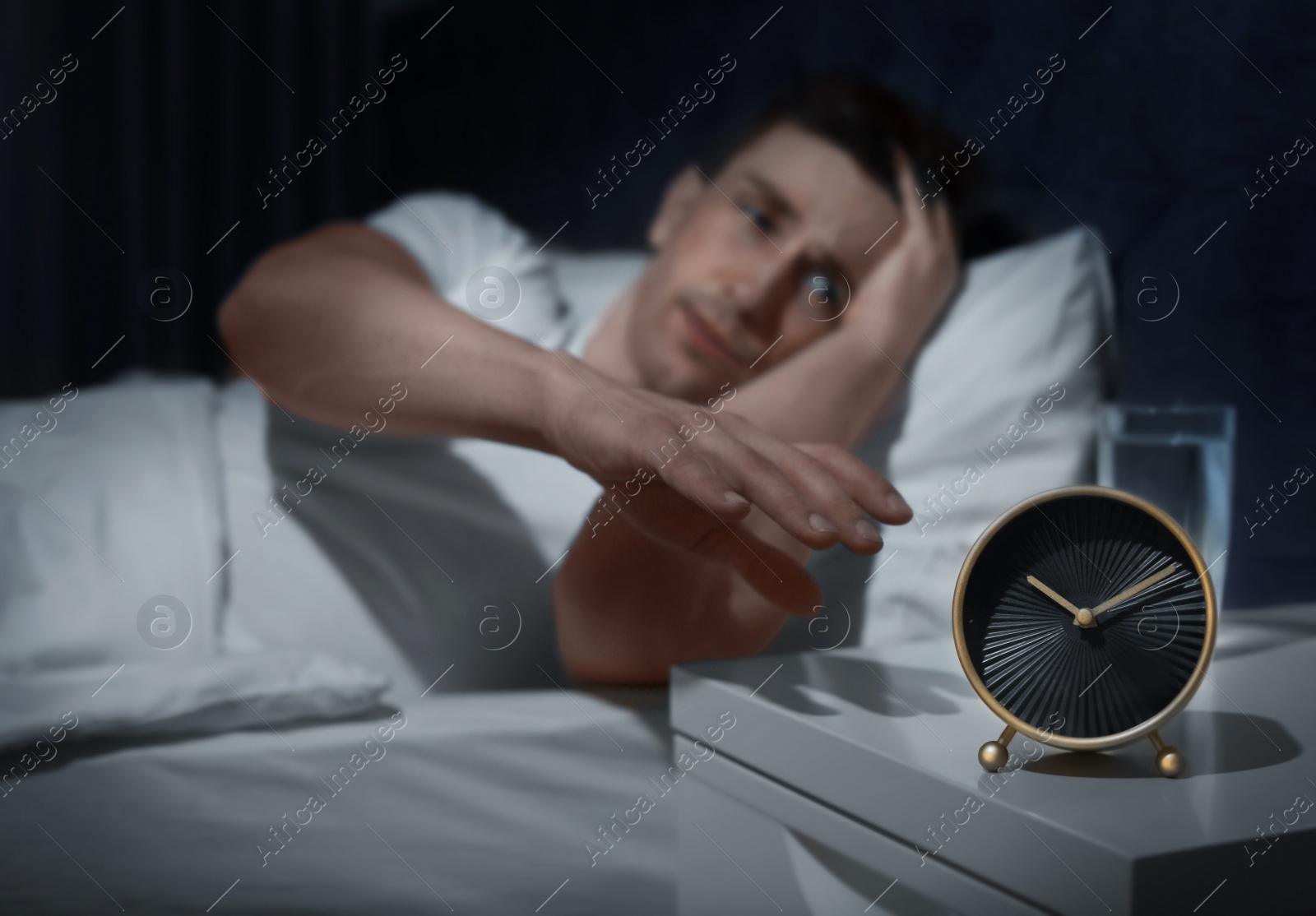 Photo of Handsome young man with terrible headache at night trying to turn off alarm clock