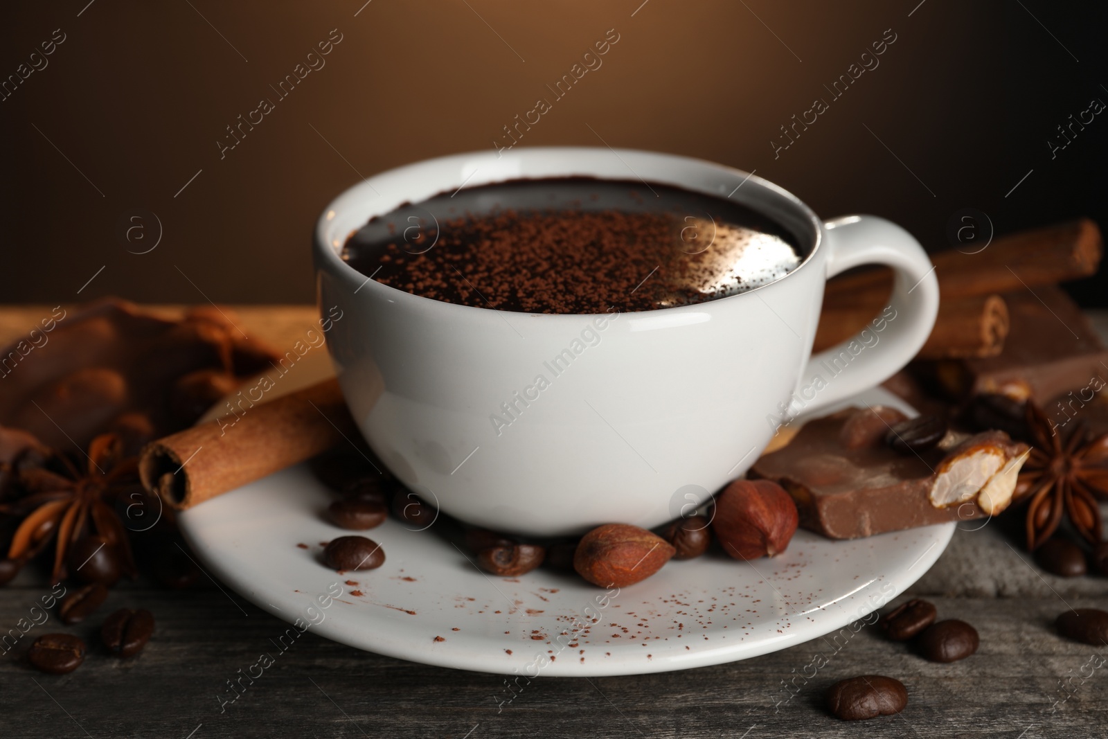 Photo of Cup of delicious hot chocolate, spices and coffee beans on wooden table