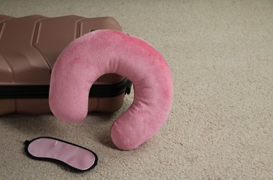 Photo of Pink travel pillow, suitcase and sleep mask on beige rug, space for text