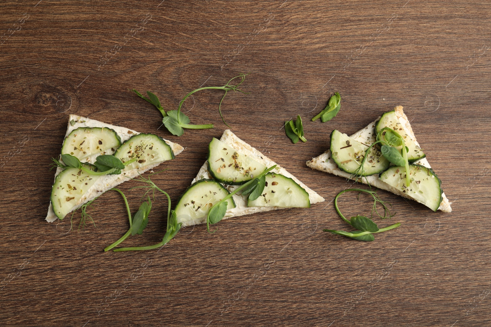 Photo of Tasty sandwiches with cream cheese, cucumber and microgreens on wooden table, flat lay