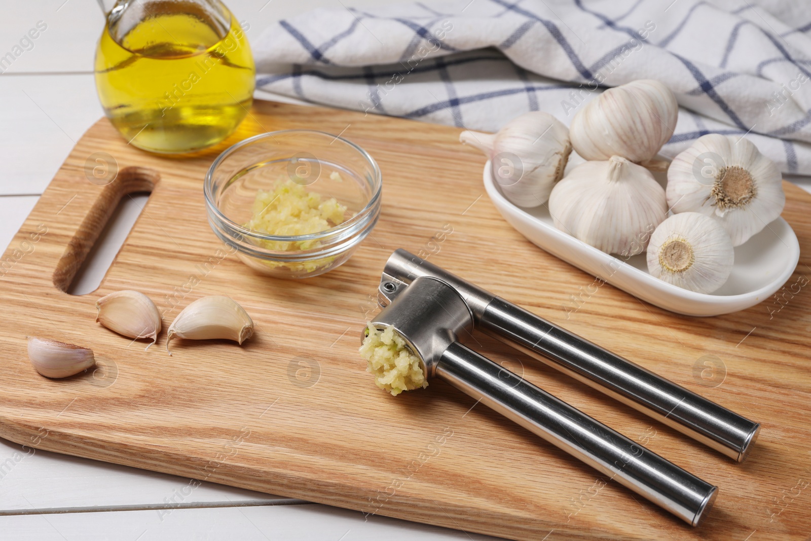 Photo of One metal press and crushed garlic on white wooden table, closeup