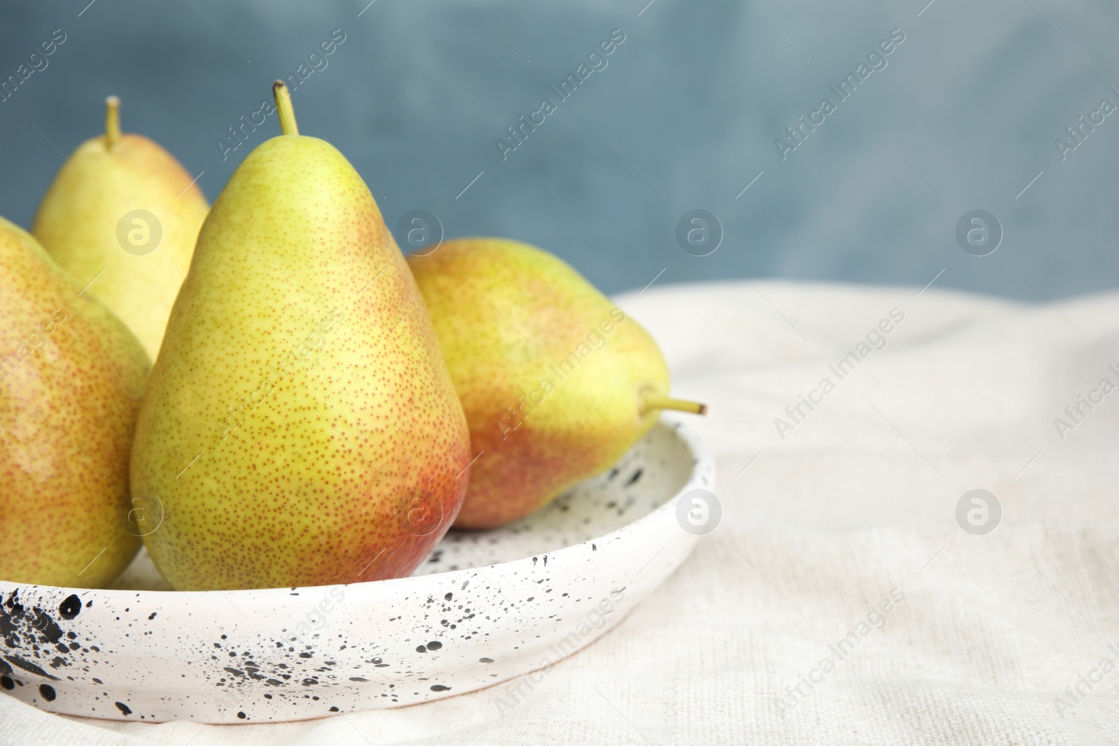 Photo of Plate with ripe juicy pears on light fabric against blue background, closeup. Space for text