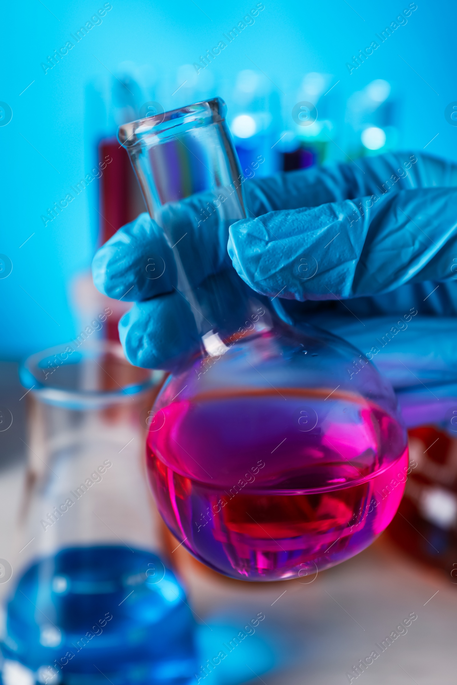 Photo of Scientist holding flask with liquid at wooden table, closeup