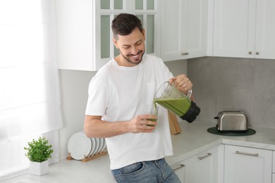 Photo of Happy man pouring delicious smoothie into glass in kitchen