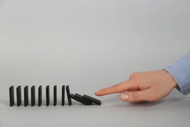 Woman causing chain reaction by pushing domino tile on grey background, closeup. Space for text