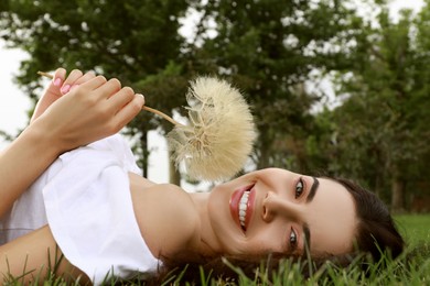 Photo of Beautiful young woman with large dandelion lying on green grass in park. Allergy free concept