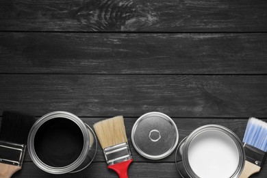 Cans of white and black paints with brushes on wooden table, flat lay. Space for text