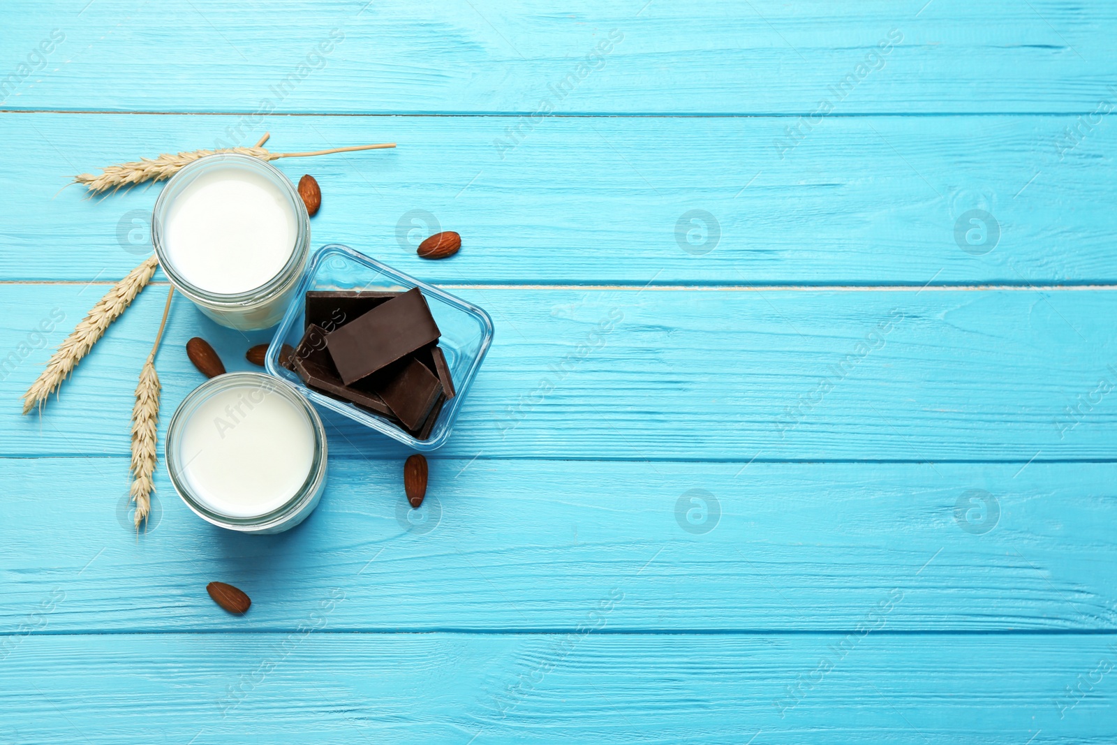 Photo of Glasses with milk, nuts and chocolate pieces on color wooden background, top view