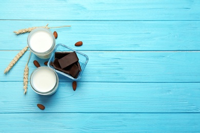 Glasses with milk, nuts and chocolate pieces on color wooden background, top view