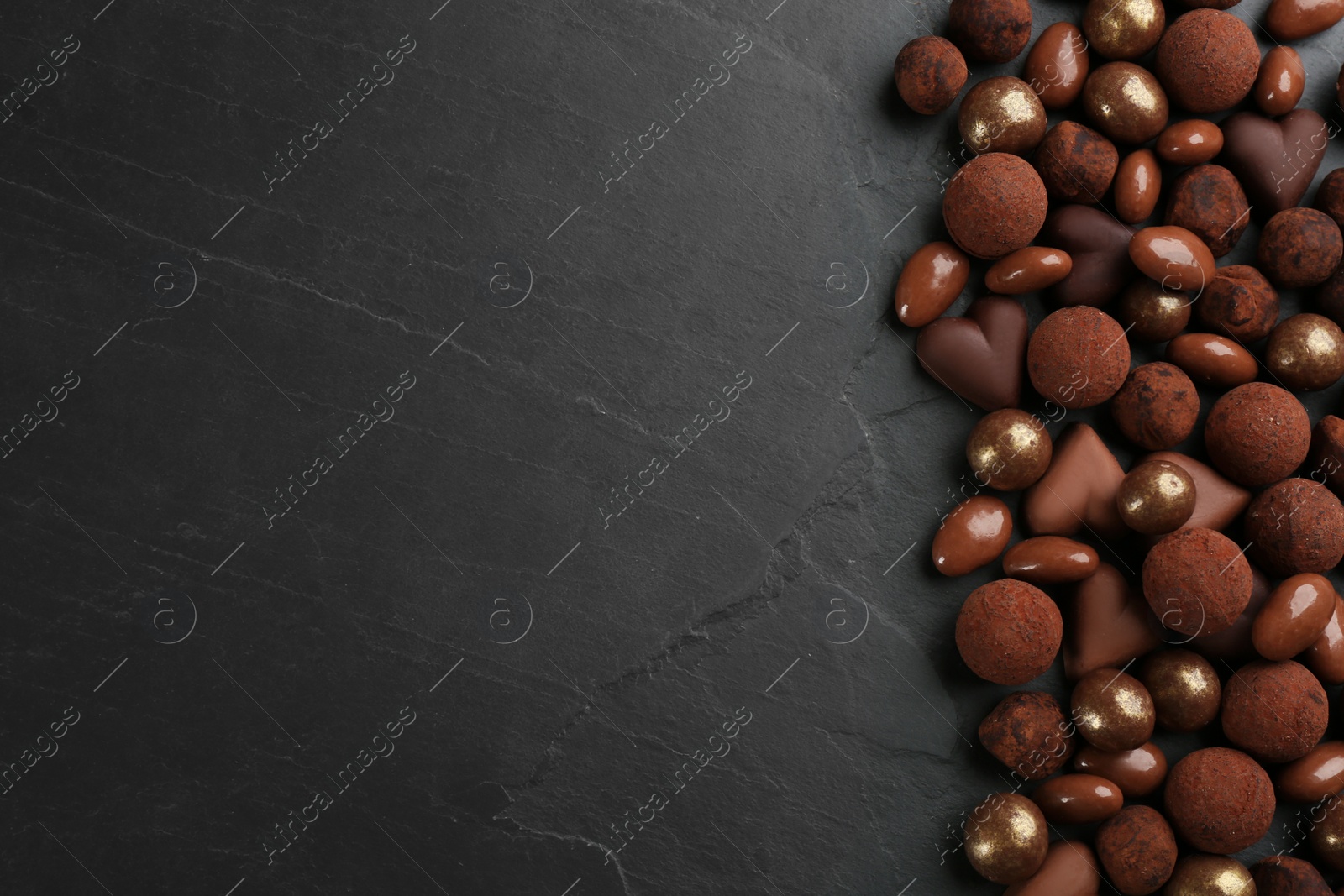 Photo of Different delicious chocolate candies on black table, flat lay. Space for text