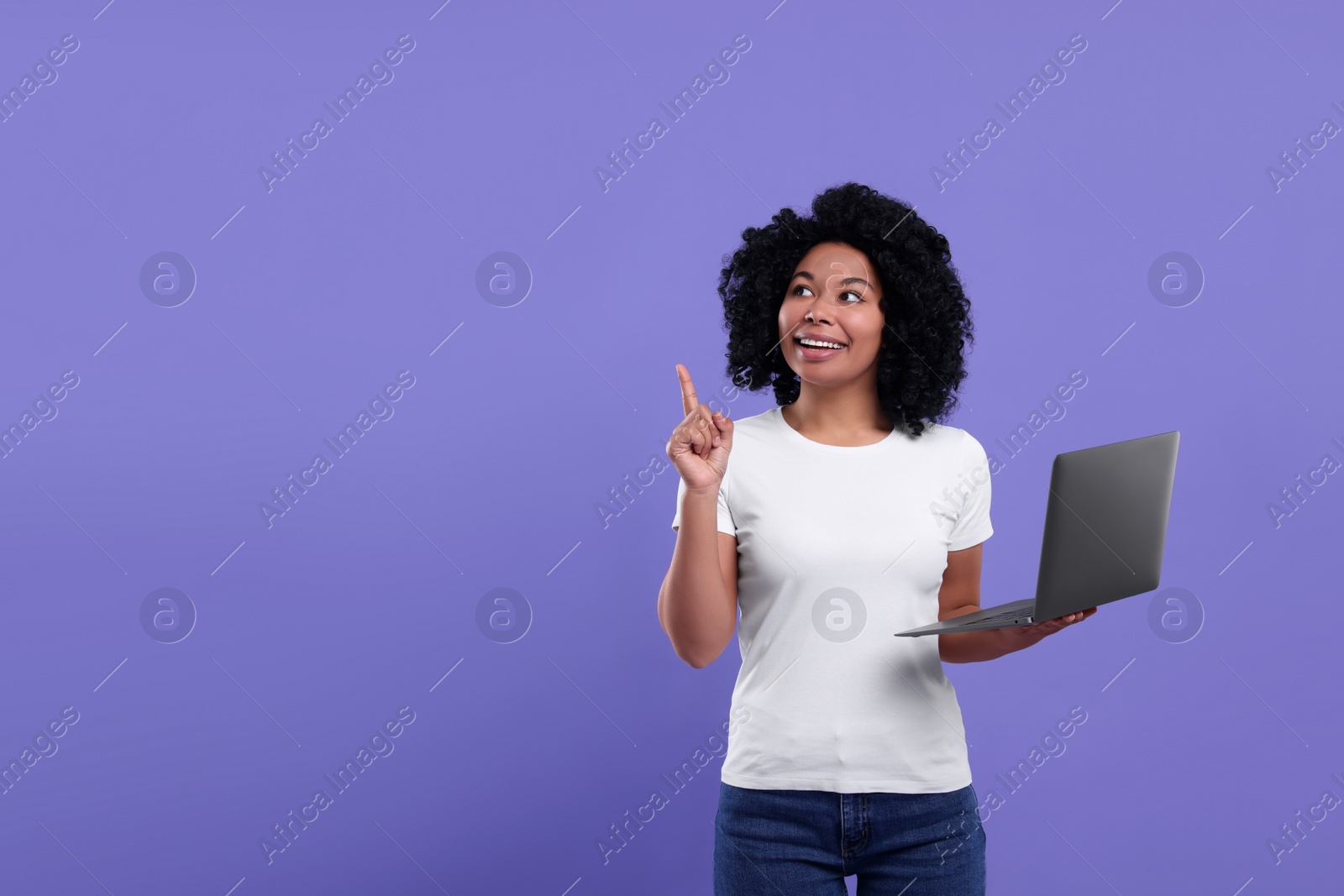 Photo of Happy young woman with laptop pointing at something on purple background. Space for text