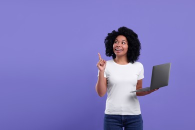 Happy young woman with laptop pointing at something on purple background. Space for text