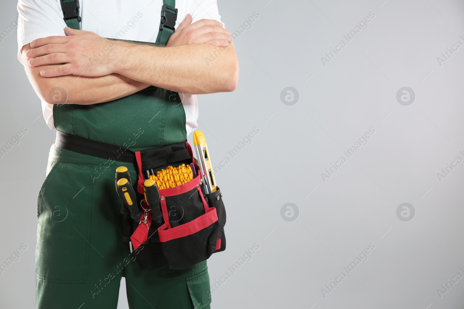 Photo of Professional construction worker with tool belt on grey background, closeup. Space for text