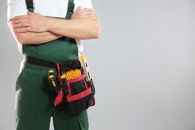 Professional construction worker with tool belt on grey background, closeup. Space for text