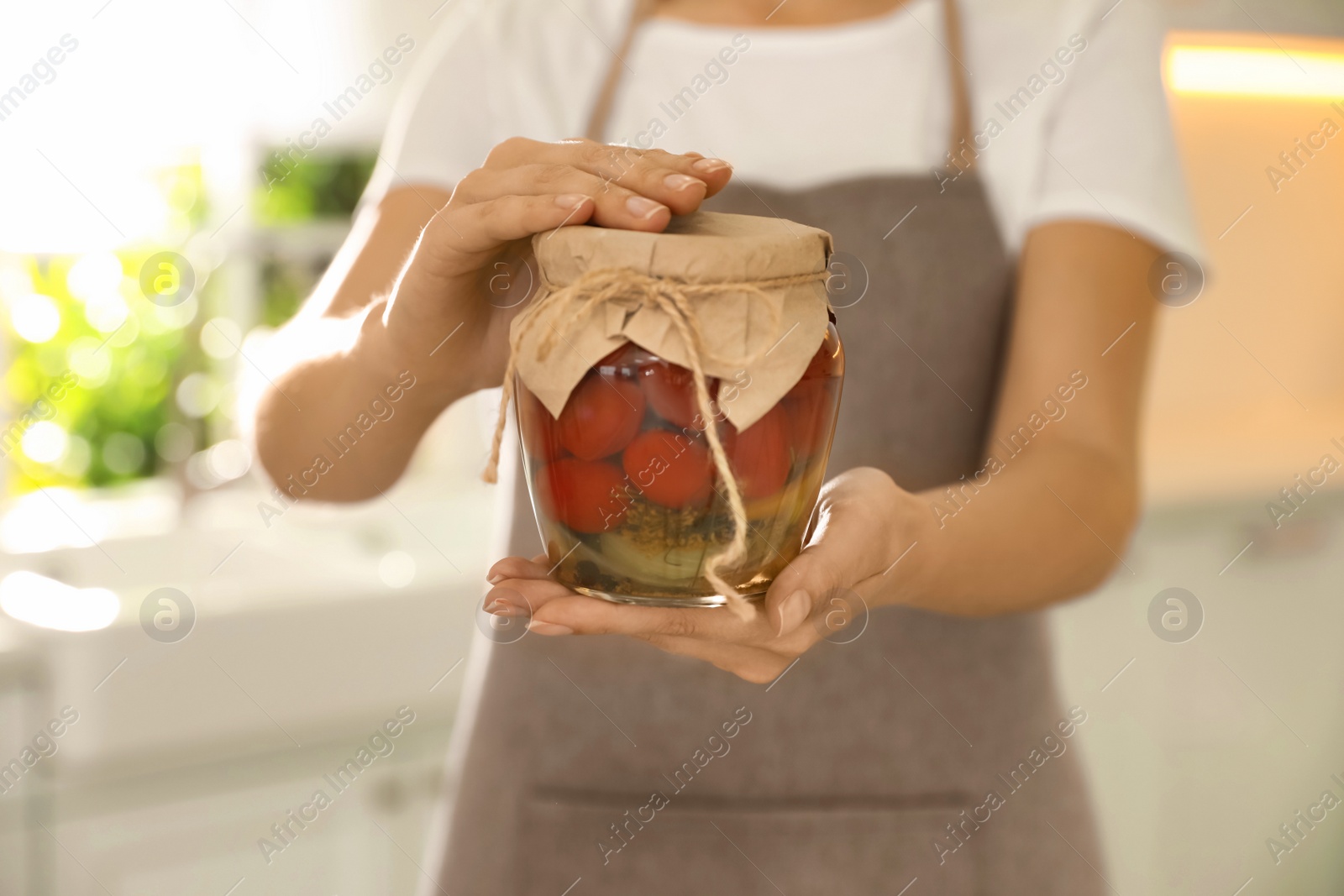 Photo of Woman holding jar of pickled tomatoes indoors, closeup