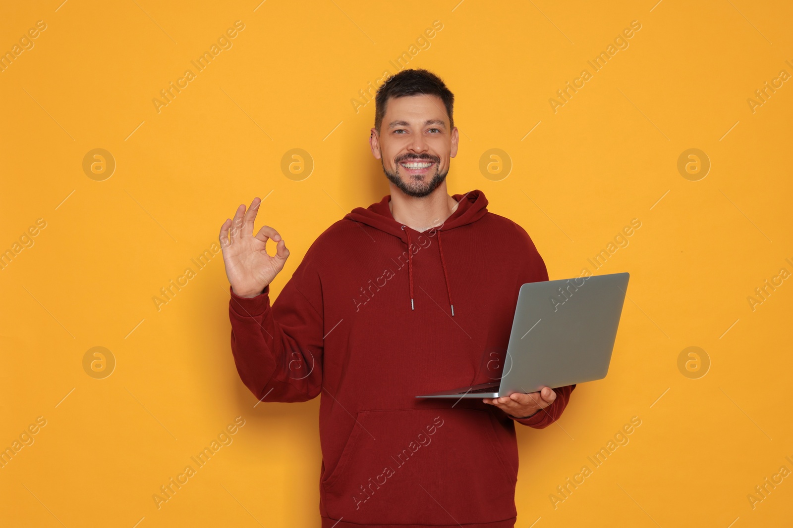 Photo of Smiling man with laptop showing okay gesture on orange background