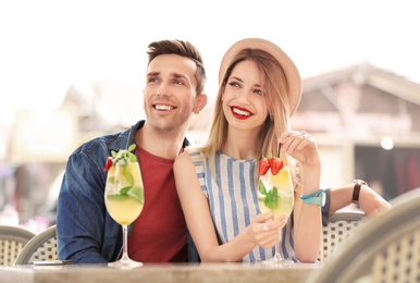 Young couple with glasses of tasty lemonade in open-air cafe