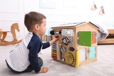Photo of Little boy playing with busy board house on floor at home