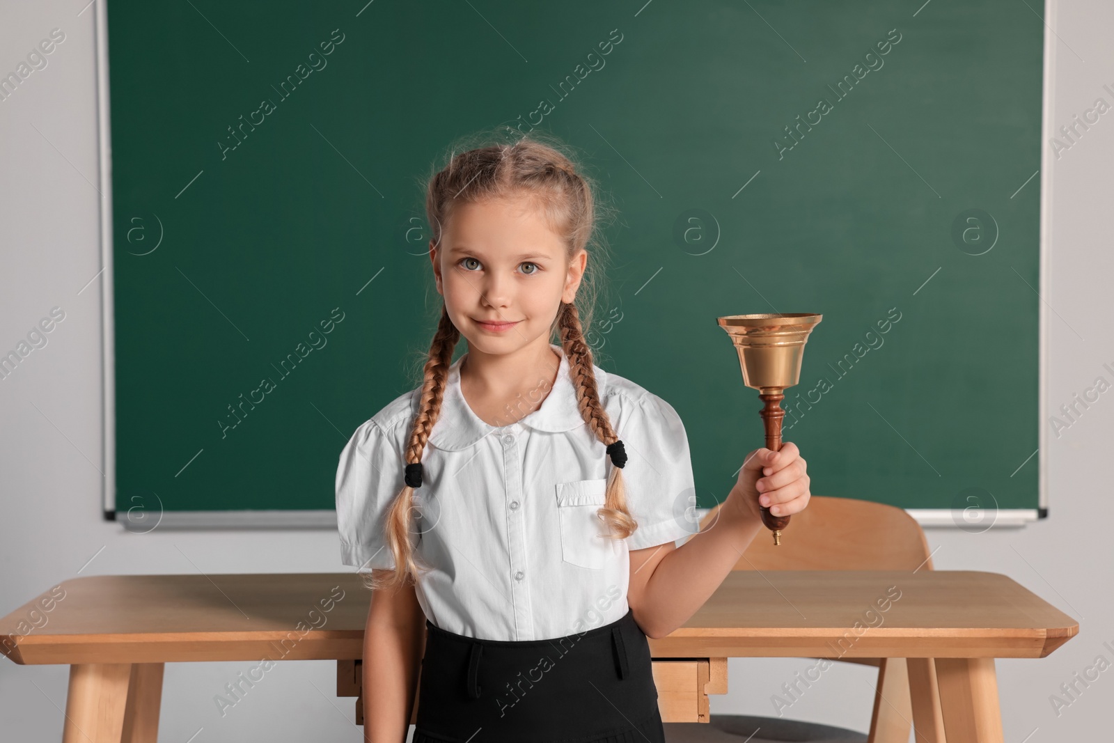 Photo of Pupil with school bell near chalkboard in classroom