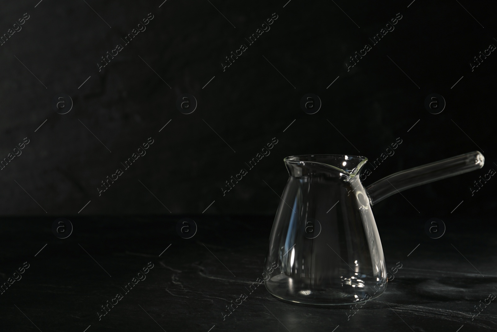 Photo of Empty glass turkish coffee pot on black table. Space for text