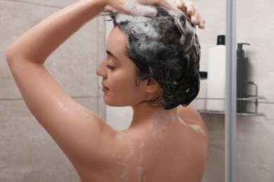 Photo of Beautiful woman washing hair with shampoo in shower, back view