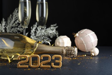 Photo of Happy New Year 2023! Bottle of sparkling wine and festive decor on table against black background