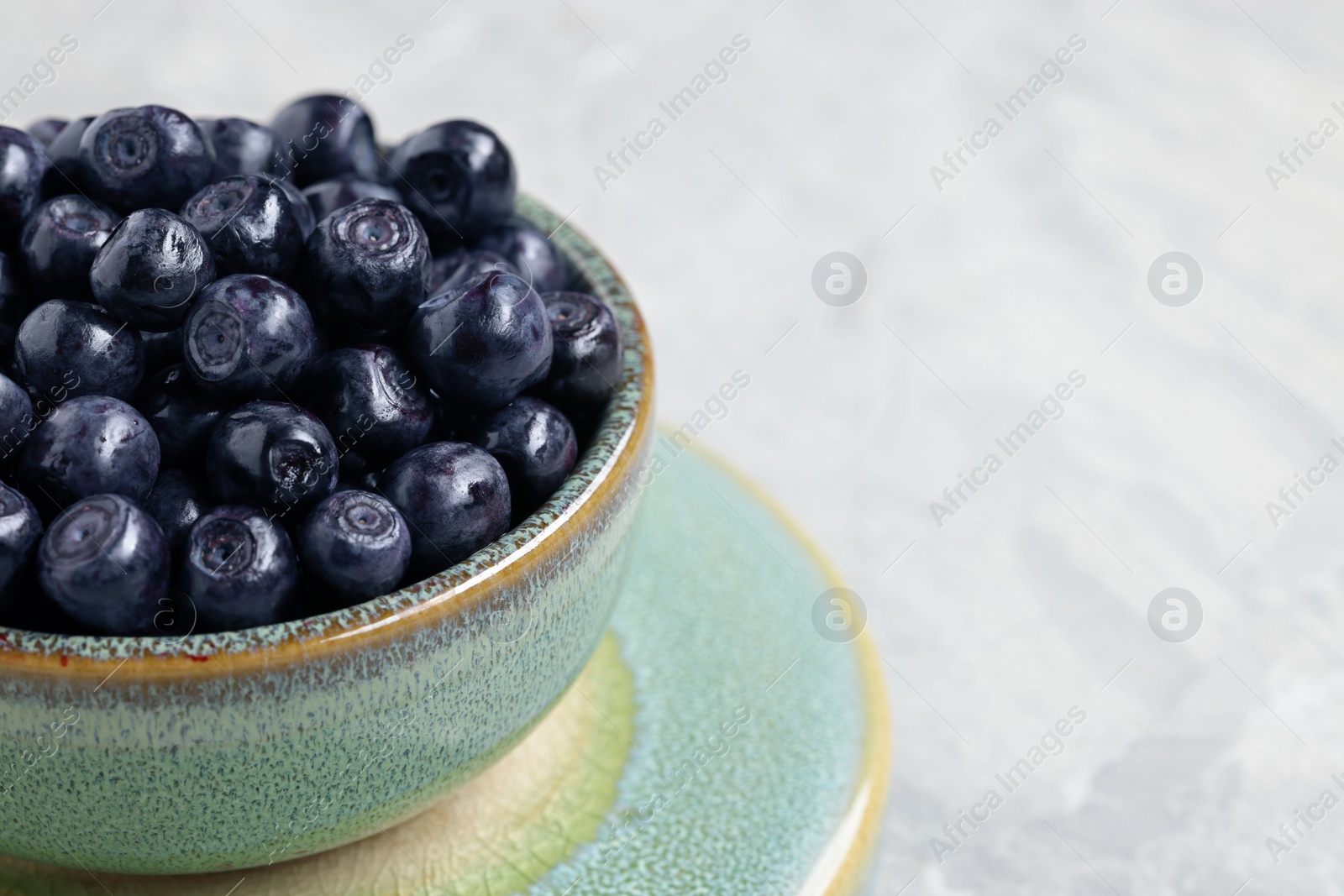 Photo of Tasty fresh bilberries in bowl on white table, closeup. Space for text