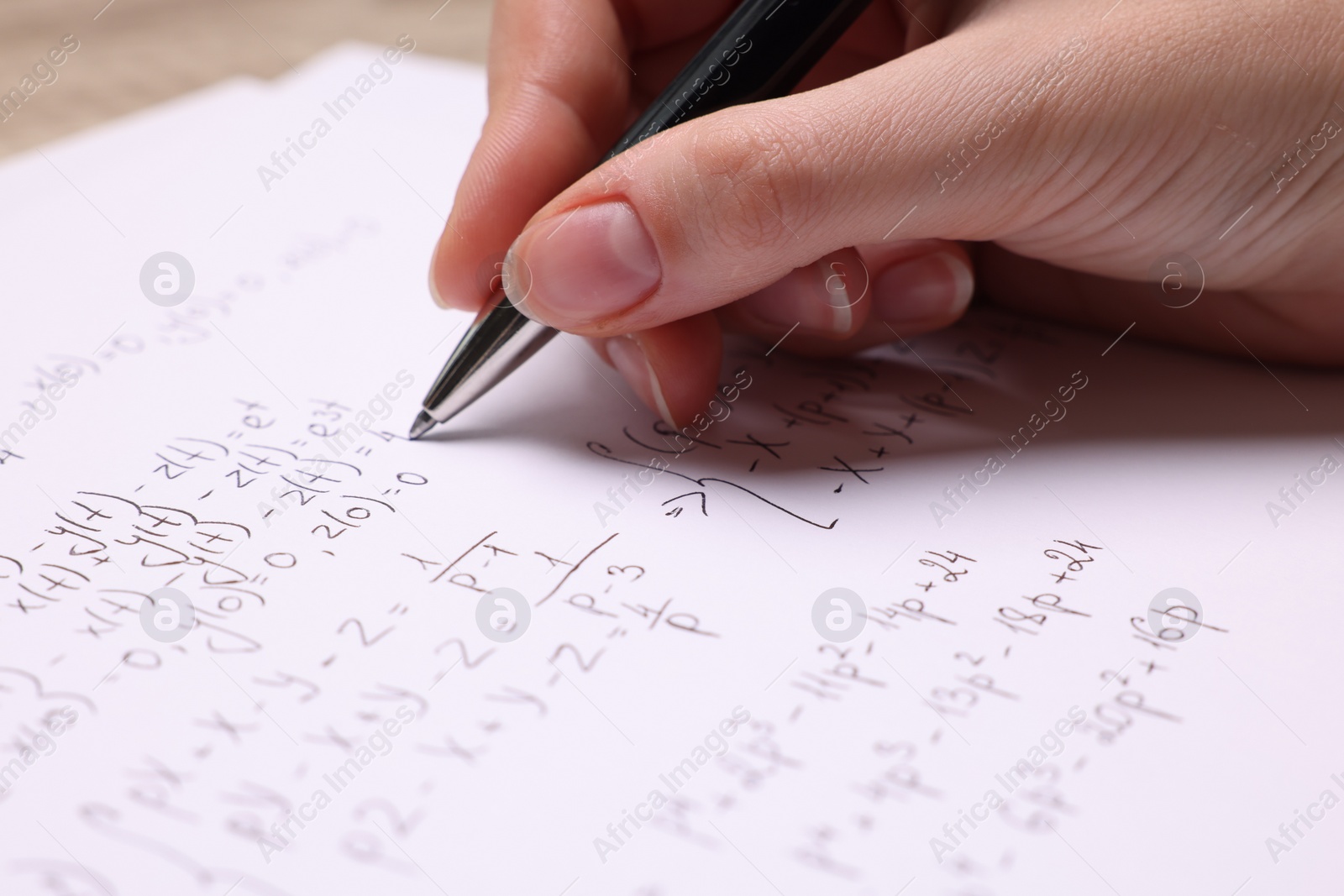 Photo of Student writing different mathematical formulas on paper, closeup