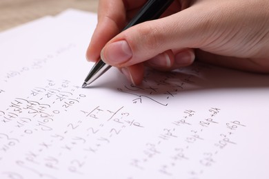 Student writing different mathematical formulas on paper, closeup