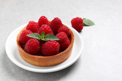 Photo of Tartlet with fresh raspberries and mint on light grey table, space for text. Delicious dessert