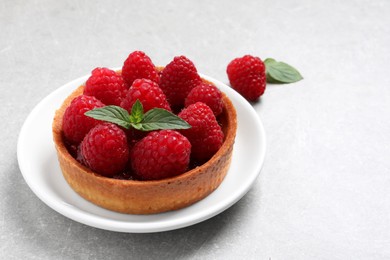 Tartlet with fresh raspberries and mint on light grey table, space for text. Delicious dessert