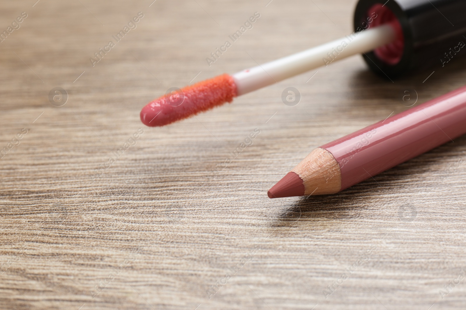 Photo of Lip pencil and brush of liquid lipstick on wooden table, closeup. Cosmetic product