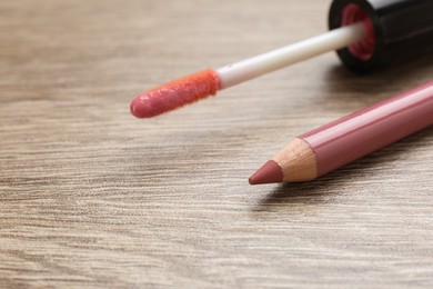 Lip pencil and brush of liquid lipstick on wooden table, closeup. Cosmetic product