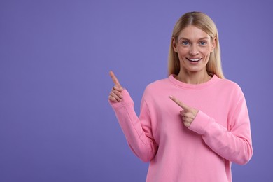Photo of Special promotion. Smiling woman pointing at something on purple background. Space for text