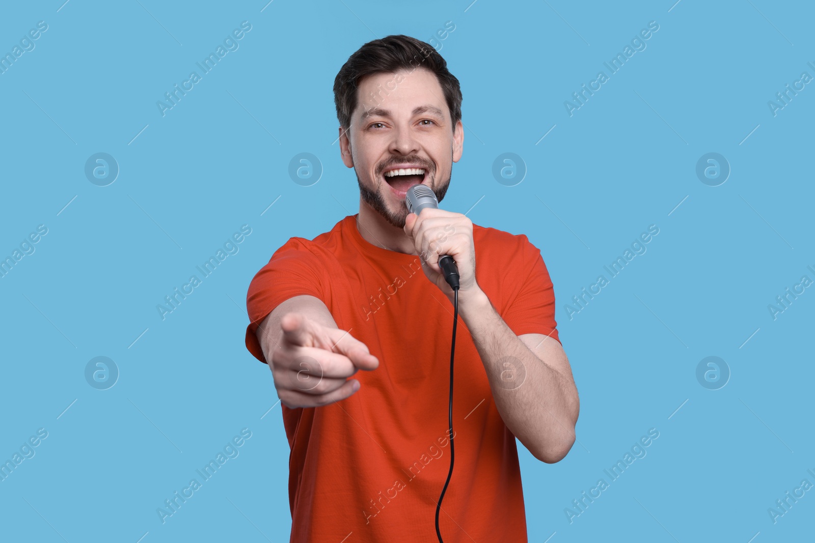 Photo of Handsome man with microphone singing on light blue background