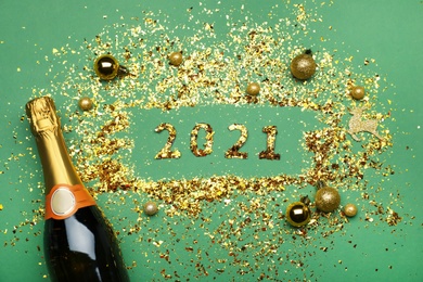 Photo of Flat lay composition with confetti, festive decor and bottle of champagne on green background. New Year celebration