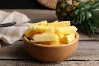 Photo of Pieces of tasty ripe pineapple in bowl on wooden table, closeup