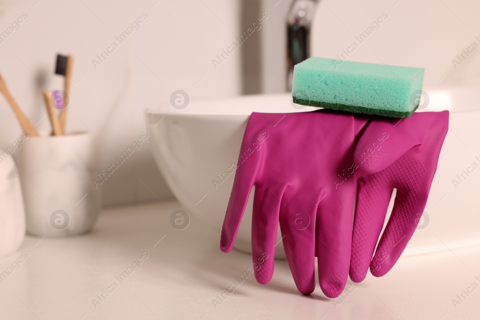 Photo of Sponge and rubber gloves on bathroom sink indoors, closeup. Space for text