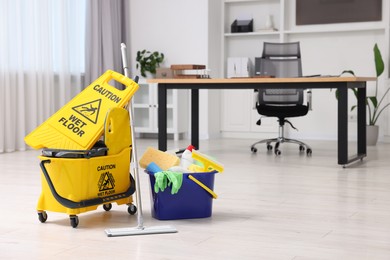 Photo of Cleaning service. Mop, bucket with supplies and wet floor sign in office, space for text